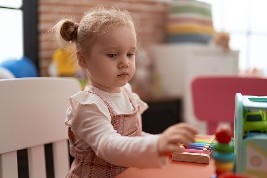 Adorable caucasian girl playing with toys sitting on table at kindergarten