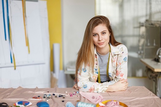 Pretty young seamstress in shirt leaning on table and dreamily l Pretty young seamstress in shirt leaning on table and dreamily l